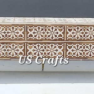 Può includere: Un mobile TV in legno bianco e marrone con quattro cassetti che presentano un motivo geometrico. Il mobile ha gambe in metallo dorato. US Crafts è stampato sulla parte anteriore del mobile.