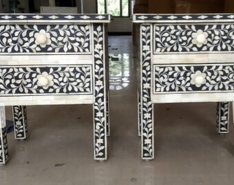 May include: Two black and white end tables with intricate floral designs made from bone inlay. Each table has two drawers with bone inlay knobs. The tables are labeled "US Crafts".