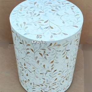 May include: A white round side table with a floral pattern made of mother of pearl inlay. The table has a white background with brown and blue floral designs.
