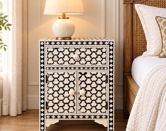 May include: A rectangular bedside table featuring a black and white geometric pattern across its single drawer and two cabinet doors. The piece includes three round, textured white knobs and stands on four short, sturdy legs with a clean finish.