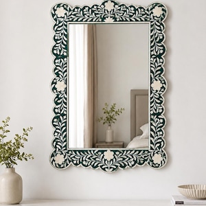May include: A rectangular wall mirror featuring a dark green scalloped frame with an intricate white floral and vine inlay pattern. The design includes symmetrical flower motifs along the edges, creating a decorative border around the glass.