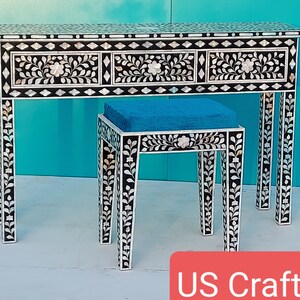 May include: A black and white vanity table and matching stool set. The table has three drawers and is decorated with floral and leaf designs. The stool has a blue cushion. The set is made with mother of pearl inlay.