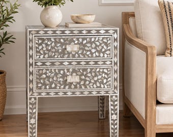 May include: A two-drawer nightstand featuring a gray finish with intricate white mother-of-pearl inlay in a leaf and diamond pattern. The piece has four straight legs with matching floral inlay and rectangular mother-of-pearl drawer pulls.