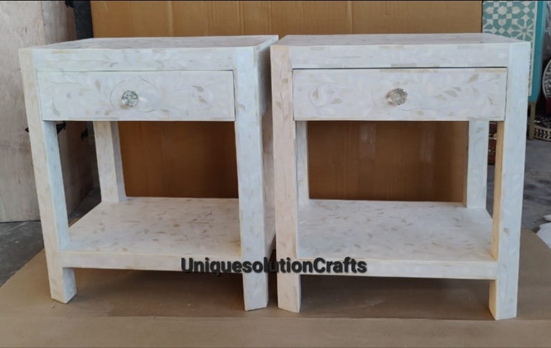 May include: Two white nightstands with a single drawer and a lower shelf. Each nightstand has a crystal-like knob on the drawer. The nightstands are made of a white material with a marbled pattern. The text "UniquesolutionCrafts" is visible on the bottom of the image.