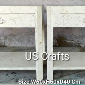 May include: Two white bedside tables with intricate floral designs and a single drawer. Each table has a lower shelf and measures 60 inches wide, 60 inches high, and 40 inches deep. The tables are made of white wood and have a polished finish. The text "US Crafts" is visible in the center of the image.
