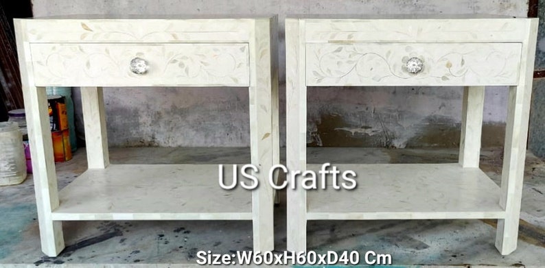 May include: Two white bedside tables with intricate floral designs and a single drawer. Each table has a lower shelf and measures 60 inches wide, 60 inches high, and 40 inches deep. The tables are made of white wood and have a polished finish. The text "US Crafts" is visible in the center of the image.
