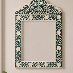 May include: A rectangular wall mirror frame featuring a dark green background with inlaid cream-coloured floral and vine patterns. The frame has a decorative arched top section and a flat base, showcasing intricate botanical motifs throughout.