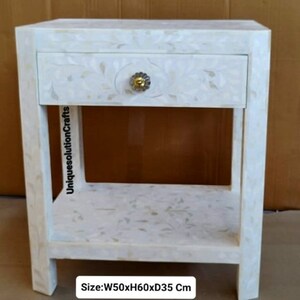 May include: White nightstand with a single drawer and a lower shelf. The drawer has a floral design and a gold knob. The nightstand measures 20 inches wide by 24 inches high by 14 inches deep. Size: W50xH60xD35 Cm