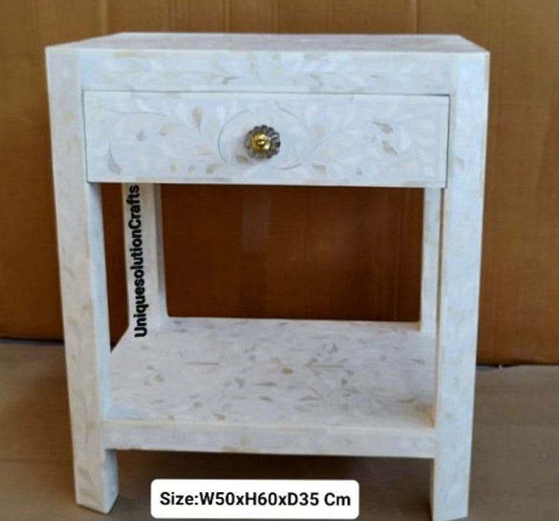 May include: White nightstand with a single drawer and a lower shelf. The drawer has a floral design and a gold knob. The nightstand measures 20 inches wide by 24 inches high by 14 inches deep. Size: W50xH60xD35 Cm