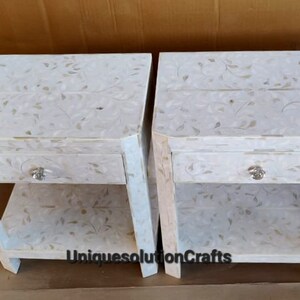 May include: Two white nightstands with a floral design and a single drawer. Each nightstand has a lower shelf. The nightstands are made of wood and have a white finish.