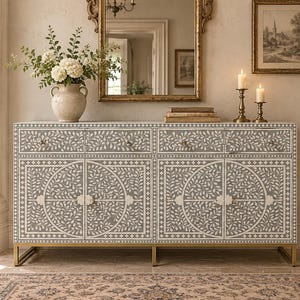 May include: A rectangular sideboard featuring a grey and white floral inlay pattern across four cabinet doors and four drawers. The piece is supported by a gold-toned metal base and includes small, round, light-colored knobs on each door and drawer.