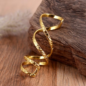 May include: A gold-toned, spiral-shaped ring with a textured design. The ring is made of metal and has a simple, elegant design.