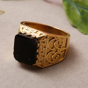 May include: A gold ring featuring a black stone and intricate detailing. The ring has a wide band with an ornate design.