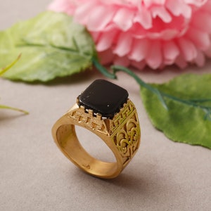 May include: A gold ring with an ornate design and a black square stone in the centre.