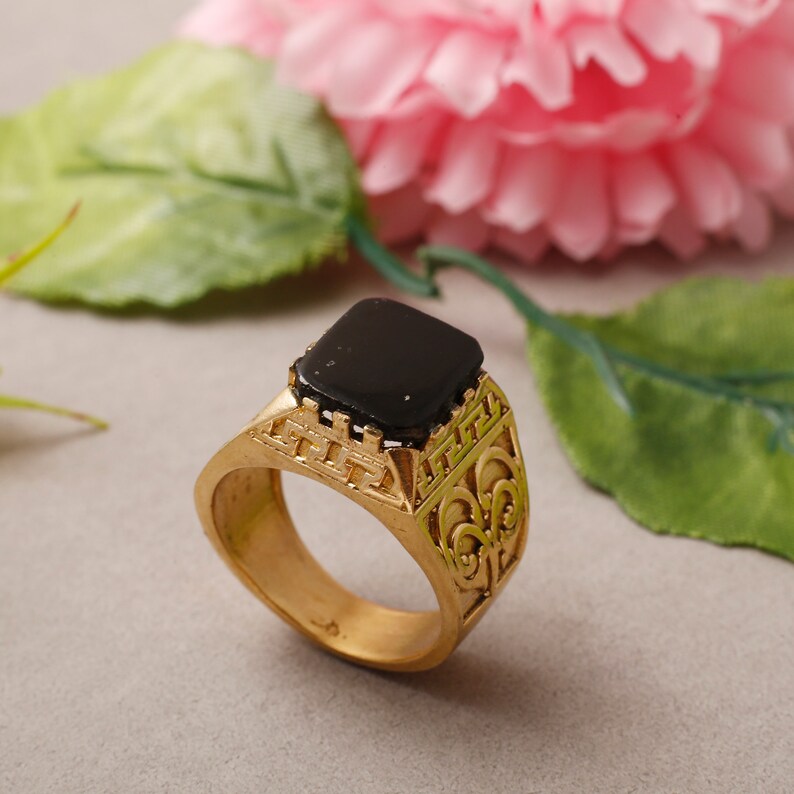 May include: A gold ring with an ornate design and a black square stone in the centre.