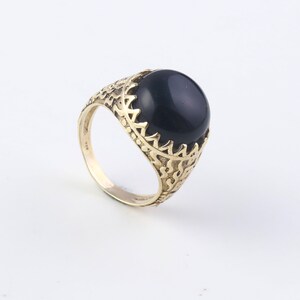 May include: A gold ring featuring a black gemstone set within an intricate, ornate design.