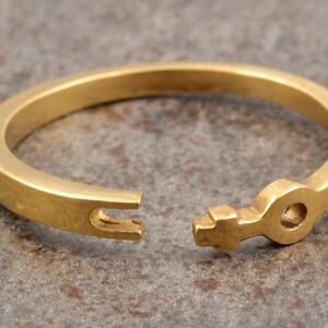 May include: A gold-toned ring with a key-shaped design. The ring is open and the key is visible.
