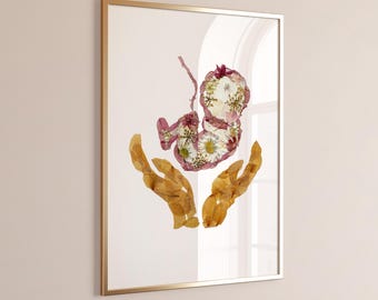 Könnte beinhalten: Ein gerahmter Wandkunstdruck mit einer Collage aus gepressten Trockenblumen, die die Form eines Fötus bilden. Der Fötus besteht aus weißen und rosa Blütenblättern, während zwei Hände, die den Fötus umschließen, aus goldbraunen getrockneten Blättern geformt sind.