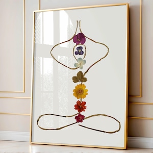 May include: A framed wall art print featuring a yoga pose silhouette constructed from thin brown twigs and pressed flowers. The central vertical axis displays a sequence of purple, blue, white, green, yellow, orange, and red flower blossoms.