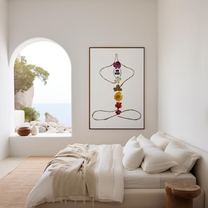 May include: A framed wall art print featuring a stylized human figure in a seated yoga pose, constructed from thin brown twigs and a vertical arrangement of seven colorful pressed flowers representing the chakras on a white background.