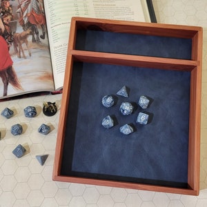 May include: A wooden dice tray with a blue felt lining. The tray has a small compartment on the top. There are several blue dice with white numbers on the felt lining.