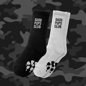 May include: A pair of black and white socks with the text "GOOD PUPS CLUB" on each sock. The socks have a paw print design on the bottom.
