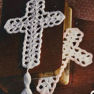 May include: Two handmade crochet cross bookmarks. One is white with a white tassel, and the other is pink with a pink tassel. The crosses are placed in a book. The image has a vintage aesthetic.