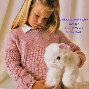 May include: A young girl wearing a pink knitted jumper with a mixed stitch pattern. The jumper has a cable knit design on the sleeves and a white collar. The girl is holding a white stuffed cat. The text on the image reads "Mr. Buntings Coat Childs Mixed Stitch Jumper 1 to 8 Years 8 Ply Knit".