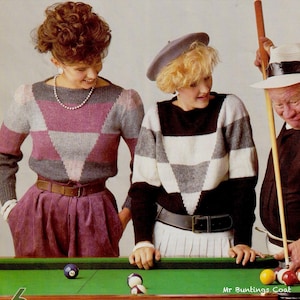 Pode incluir: Duas pessoas usando suéteres com padrões geométricos, um em tons de cinza e rosa, o outro em preto, branco e cinza. Elas estão perto de uma mesa de bilhar verde. Uma terceira pessoa está segurando um taco de bilhar.