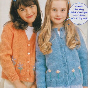 May include: Two young girls wearing knitted cardigans. One cardigan is orange with floral embroidery, the other is light blue with similar floral details. The image includes text that reads "Classic Stocking Stitch Cardigan 2-10 Years DK/ 8 Ply Knit".