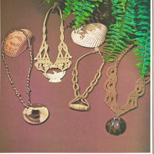 Puede incluir: Una variedad de collares hechos a mano con colgantes y conchas únicas. Los collares se exhiben sobre un fondo marrón con follaje verde y conchas marinas. El texto en la parte inferior dice "Earth & Satin", "Strings 'n Wings", "Onyx Overture" y "Shell for Mam'selle".