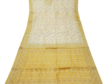 May include: A cream-coloured silk saree with a floral pattern and a gold border. The saree has a subtle shimmer and a delicate texture.