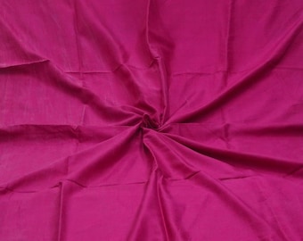 Op de afbeelding: Een effen magentakleurige stof met een gladde, matte textuur. Het materiaal is gedrapeerd in een centraal wervelpatroon, waardoor zachte, stralende plooien en schaduwen ontstaan die de diepe, levendige roze kleur over het hele oppervlak benadrukken.