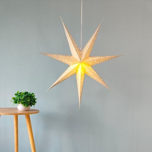 May include: A large, cream-colored star-shaped paper lantern with pointed edges hangs from a white cord. The star has small, evenly spaced holes that emit a warm, yellow light. The star is a decorative element.