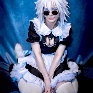 May include: A black and white maid outfit featuring a cat-themed chest cutout, white ruffled trim, and a matching white wig with cat ears. The ensemble includes round black sunglasses, white thigh-high stockings, and a white tail accessory.