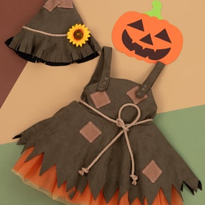 Può includere: Un costume da spaventapasseri marrone e arancione per un bambino. Il costume include un vestito con un corpetto marrone e una gonna di tulle arancione, un cappello marrone con un girasole e un ritaglio di carta a forma di zucca.