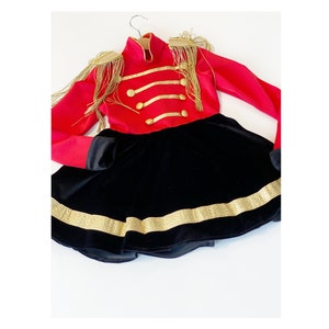 May include: A red and black costume with gold trim and buttons. The top has long sleeves and gold fringe on the shoulders. The skirt is black velvet with a gold band around the bottom.