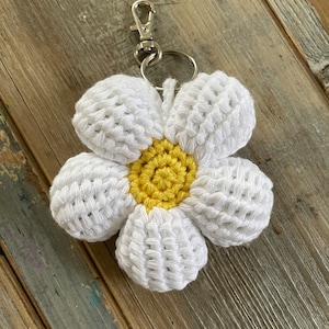 Op de afbeelding: Witte gehaakte bloemen sleutelhanger met een geel centrum. De sleutelhanger heeft een zilveren metalen ring en sluiting.