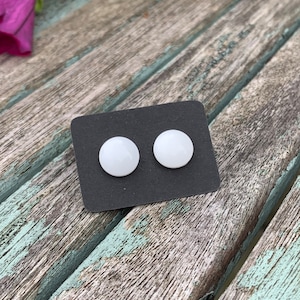 May include: A pair of white round stud earrings displayed on a black card.
