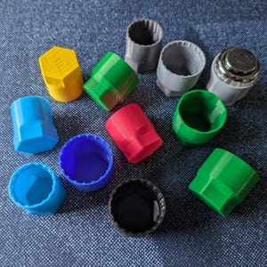 May include: Assortment of colourful plastic caps in various shapes and sizes, including blue, green, red, yellow, and grey. Some caps have a hexagonal shape, while others are round.