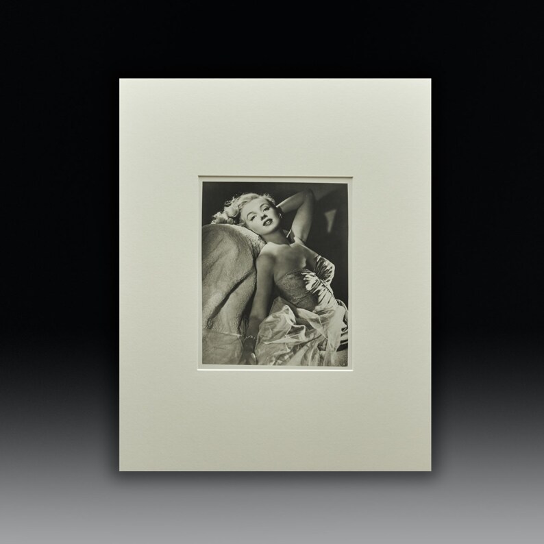 Puede incluir: Fotograf&iacute;a en blanco y negro de una mujer con un vestido sin tirantes, reclinada en una silla. Ella est&aacute; mirando a la c&aacute;mara con una sonrisa suave.