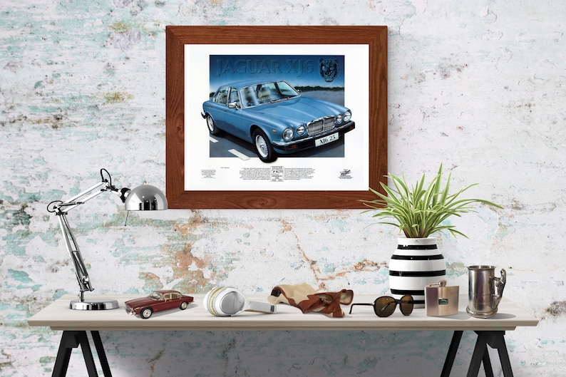 May include: A framed print of a blue Jaguar XJ6 car with the text "JAGUAR XJ6" and "XJB 25" on the car. The print is on a white background and has a brown wooden frame.