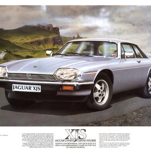 May include: A silver Jaguar XJS Grand Tourer car is parked on a winding road with a mountainous backdrop. The car has a black grille and black trim around the windows. The text "JAGUAR XJS" is visible on the front of the car. The text "XJS JAGUAR'S FINEST GRAND TOURER ALWAYS CONTROVERSIAL, THE XJS PLACED IT'S OWN UNCOMPROMISING STAMP ON THE FACE OF GRAND TOURING" is visible at the bottom of the image.