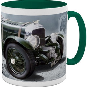May include: A green and silver vintage Bentley race car with a number plate that reads "GY 3905". The car is on a grey background with a blurred image of a man in a racing helmet in the background.