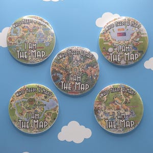Può includere: Cinque spille rotonde con illustrazioni colorate di mappe di parchi a tema. Ogni spilla riporta il testo "WHO NEEDS A MAP?" in alto e "I AM THE MAP" in basso, con caratteri bianchi, spessi e contornati su mappe dettagliate.