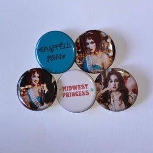 Könnte beinhalten: Fünf runde Buttons. Ein Button ist türkis mit dem Text "CHAPPELL ROAN". Zwei Buttons zeigen eine Frau mit roten Haaren. Ein Button ist weiß mit "MIDWEST PRINCESS" und einem grünen Stern. Die Buttons liegen auf einer weißen Oberfläche.