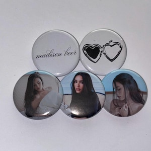 May include: A collection of five round buttons. One button has the text "madison beer" in a script font. Another button features a heart-shaped locket design. The remaining three buttons display images of a woman.