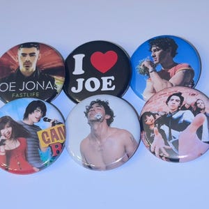 Könnte beinhalten: Eine Sammlung von sechs runden Ansteckbuttons. Die Buttons zeigen Bilder von männlichen Prominenten, darunter Joe Jonas, und den Text "I ❤️ JOE". Die Buttons sind in verschiedenen Farben, darunter Schwarz, Blau und Rot.