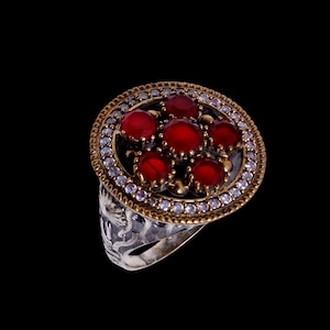 May include: A silver ring with a round red gemstone setting surrounded by smaller white gemstones.