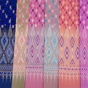 May include: A collection of colorful patterned textiles. The fabrics display a repeating geometric design with diamond and square motifs. Colors include orange, blue, pink, and red. The textiles have a decorative border with a detailed pattern.